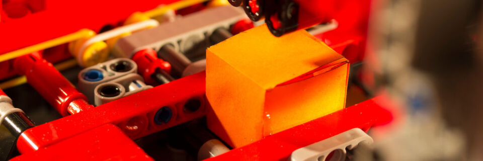 Mithilfe der Lego Mindstorms Technologie schneidet, faltet und klebt die Papercube-Anlage aus einem Stück Papier vollautomatisch einen Würfel. Mithilfe der Lego Mindstorms Technologie schneidet, faltet und klebt die Papercube-Anlage aus einem Stück Papier vollautomatisch einen Würfel.