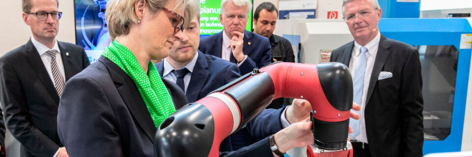 Lukas Nikelowski (Fraunhofer-IML) hilft Ministerin Karliczek bei der Bedienung eines Roboterarms. Im Hintergrund (v.l.): Prof. Dr. Georg Rosenfeld, Ullrich Sierau, Georgios Katsimitsoulias und Prof. Dr. Michael ten Hompel. Lukas Nikelowski (Fraunhofer-IML) hilft Ministerin Karliczek bei der Bedienung eines Roboterarms. Im Hintergrund (v.l.): Prof. Dr. Georg Rosenfeld, Ullrich Sierau, Georgios Katsimitsoulias und Prof. Dr. Michael ten Hompel.