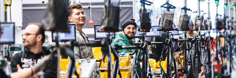 Per OCS werden die Fahrradrahmen zu den einzelnen Stationen transportiert. Die hier einzubauenden Einzelteile in Kisten mit QR-Codes gelangen per Kommissionswagen zu den Arbeitsplätzen. Jedes Teil ist jeweils nur für einen Auftrag bestimmt. Per OCS werden die Fahrradrahmen zu den einzelnen Stationen transportiert. Die hier einzubauenden Einzelteile in Kisten mit QR-Codes gelangen per Kommissionswagen zu den Arbeitsplätzen. Jedes Teil ist jeweils nur für einen Auftrag bestimmt.