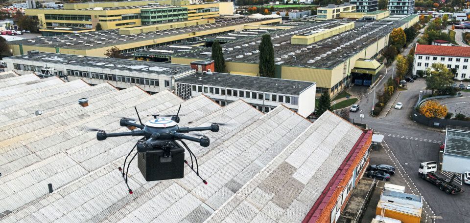 Erste automatisierte Werksdrohne in Deutschland: Eine automatisierte Lieferdrohne über den Dächern der Werkshallen des ZF-Werks 2 in Friedrichshafen. Sie bringt ein dringend benötigtes Ersatzteil auf dem Luftweg in die Instandhaltungswerkstatt. Erste automatisierte Werksdrohne in Deutschland: Eine automatisierte Lieferdrohne über den Dächern der Werkshallen des ZF-Werks 2 in Friedrichshafen. Sie bringt ein dringend benötigtes Ersatzteil auf dem Luftweg in die Instandhaltungswerkstatt.
