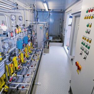 Innenansicht einer Ammoniak-Dosierstation mit zehn Kolbenmembran-Pumpen. Ganz hinten befindet sich eine Aufstellfläche für den IBC. Von dort wird die Ammoniaklösung per Deionatstrom in den Ansetzbehälter (Mitte) gesaugt und dabei verdünnt. IBC-Gestell, Ansetzbehälter und Dosierpumpen befinden sich in einer gemeinsamen Auffangwanne mit Leckagesensor. Innenansicht einer Ammoniak-Dosierstation mit zehn Kolbenmembran-Pumpen. Ganz hinten befindet sich eine Aufstellfläche für den IBC. Von dort wird die Ammoniaklösung per Deionatstrom in den Ansetzbehälter (Mitte) gesaugt und dabei verdünnt. IBC-Gestell, Ansetzbehälter und Dosierpumpen befinden sich in einer gemeinsamen Auffangwanne mit Leckagesensor.